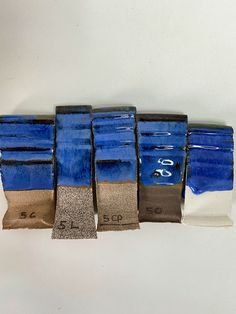 five blue and brown vases are lined up on a white surface, one is empty