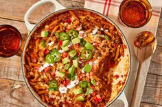 a large pot filled with pasta and sauce on top of a wooden table next to two glasses