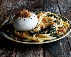 a plate topped with pasta covered in cheese and spinach next to a fork on top of a wooden table