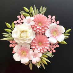 an arrangement of paper flowers on a black surface with green leaves and pink blooms in the center