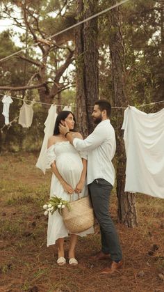 a man and woman standing next to each other in the woods with clothes hanging on a line