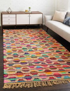 a multicolored rug with fringes on the floor in front of a white couch