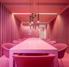 a long white table with pink chairs in a room that has vertical blinds on the walls