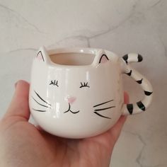 a hand holding a white ceramic cat mug