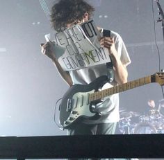 a man holding a cell phone while standing in front of a microphone and guitar on stage