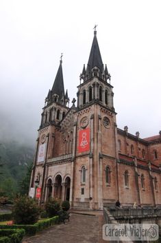 an old building with two towers on the top and one at the bottom, surrounded by greenery