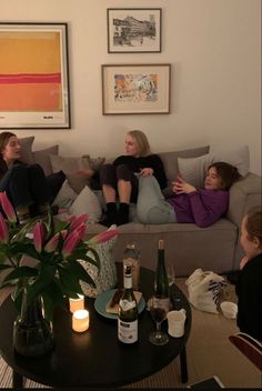 three women sitting on a couch with bottles of wine in front of them and two candles