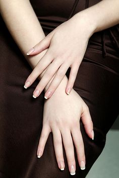 a woman's hands with white manicures sitting on her lap and wearing a brown dress