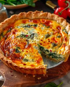 a quiche with cheese and spinach is on a wooden platter next to tomatoes