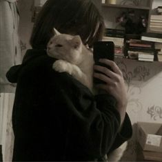 a woman holding a cat in her arms while taking a selfie with her cell phone