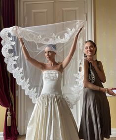 two women in dresses and veils standing next to each other with their arms raised