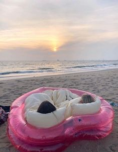 two people laying on an inflatable mattress on the beach at sunset or dawn