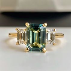 an emerald and diamond three stone ring on a white surface with gold trimmings