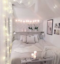 a white bedroom with string lights on the ceiling and bed in the corner, all lit up by candles