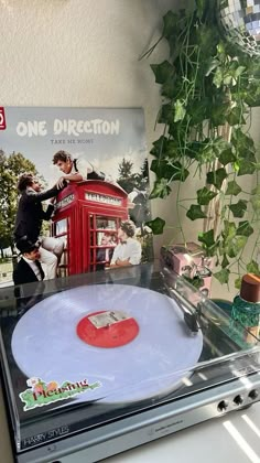 a record player sitting on top of a table next to a plant and an album