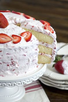 a strawberry cake with white frosting and fresh strawberries on the top is ready to be eaten