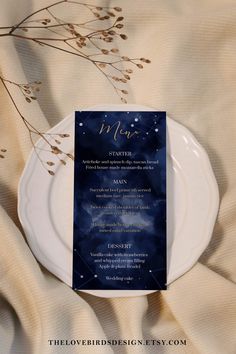 a white plate topped with a menu on top of a cloth covered table next to a plant