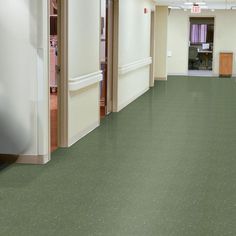 an empty room with green flooring and white walls in the center is a door leading to another room