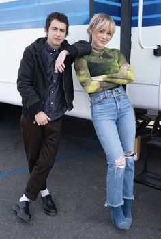 two people standing next to each other in front of a bus