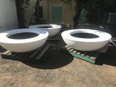 three large white bowls sitting on top of pallets in front of a building with trees