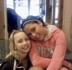 two young women sitting next to each other in front of a window and smiling at the camera