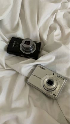 a digital camera sitting on top of a white bed sheet next to an unmade pillow