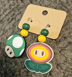 two earrings are sitting on the ground next to a tag with an image of a mushroom