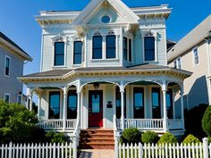 a large white house with a red door and two story front porch on a sunny day