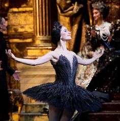 the ballerina is dressed in black and has her arms spread out as she stands on stage