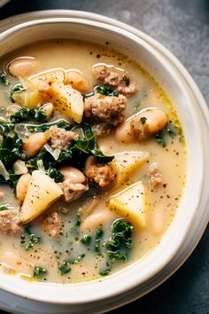 a white bowl filled with soup and meatballs on top of a table next to a spoon