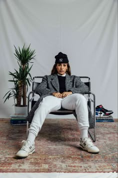 a woman sitting in a chair with her legs crossed and wearing a black beanie