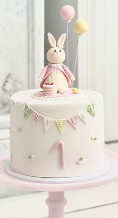 a white cake with pink frosting and bunting on the top is decorated with an animal figurine