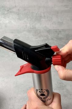 two hands are holding a red and black cup with scissors in it, while another hand holds a lighter