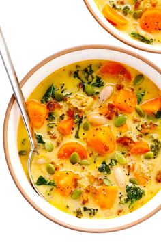 two bowls of soup with carrots, peas and broccoli in them on a white surface