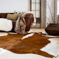 a brown and white cowhide rug on the floor next to a leather couch with pillows