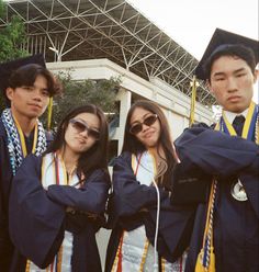 three young people in graduation gowns posing for a photo with their arms around each other