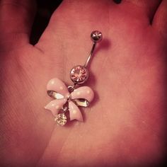 a hand holding a pink and white flower belly ring