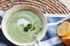 a white bowl filled with broccoli soup next to sliced oranges