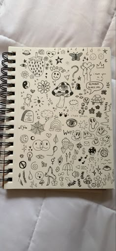 a notebook with doodles on it sitting on top of a white bed spreader