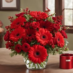 a glass vase filled with red flowers on top of a table next to a can