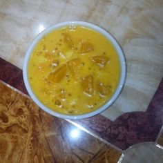 a white bowl filled with yellow liquid on top of a wooden table next to a marble floor