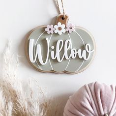 a wooden sign that says willow hanging on a wall next to some feathers and a pillow