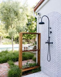 an outdoor shower with plants growing in it and a wooden shelf on the outside wall