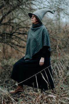 a woman wearing a gray hat and black dress is sitting in the middle of a field