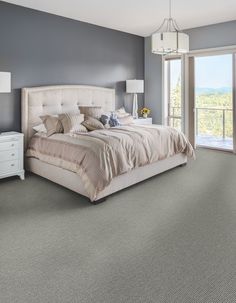 a bedroom with gray walls and carpeted flooring, a bed in the foreground