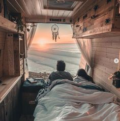 a person laying in bed looking out at the ocean from inside a truck with its door open