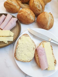 bread, ham and cheese are on plates next to rolls