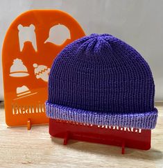 a purple knitted hat sitting on top of a wooden table next to an orange comb