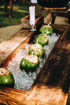 some green apples are sitting on ice in a wooden box with straws and candles