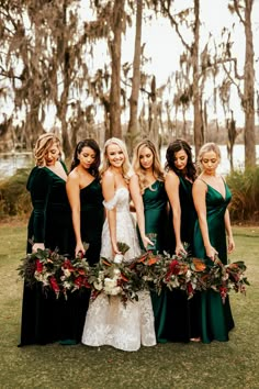 the bride and her bridesmaids pose with their bouquets in front of trees